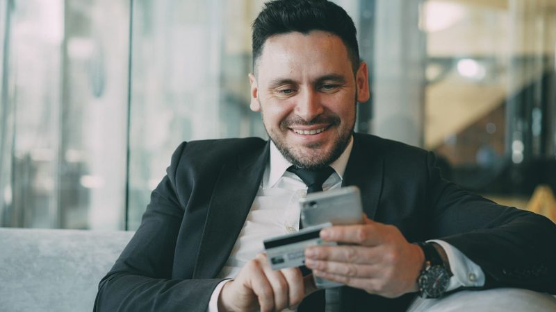 Hombre sonriente realizando un pago digital con su teléfono móvil y una tarjeta bancaria