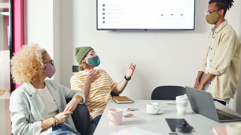 Equipo de trabajo con tapabocas discutiendo nuevas ideas de negocio en una oficina
